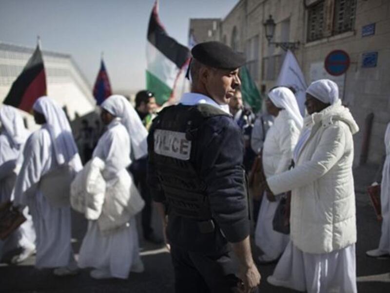 A Palestinian policeman stands guard as Nigerian worshippers cross a street near the Church of the Nativity in the Biblical West Bank city of Bethlehem, believed to be the birthplace of Jesus Christ, in the West Bank town of Bethlehem, as the Holy Land prepares to mark Christmas.	