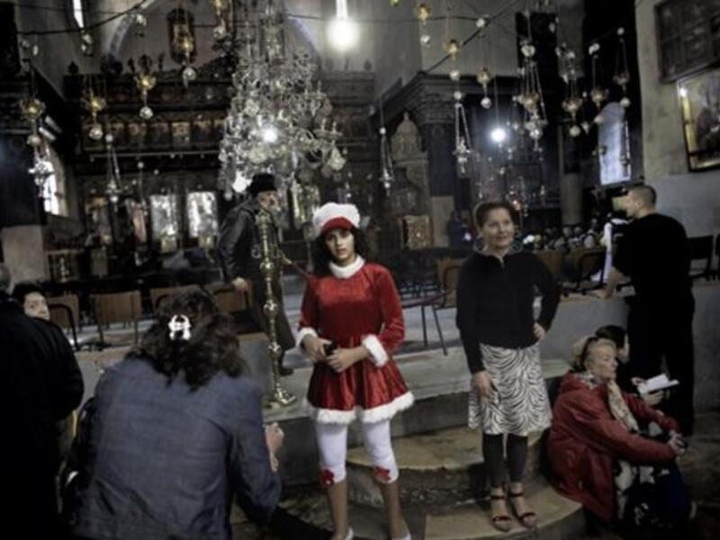 A Palestinian girl dressed in a Santa Claus attire poses alongside other worshippers inside the Church of the Nativity in the West Bank city of Bethlehem, as Christian flock to the what they believe is the birth place of Jesus Christ to celebrate his birth during Christmas mass.