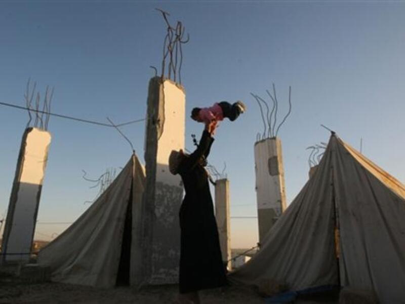 A displaced Palestinian woman carries her child outside their tent, in the Ezbet Abed Rabbo area, that was heavily destroyed during Israel's 22-day offensive on the Gaza Strip.
