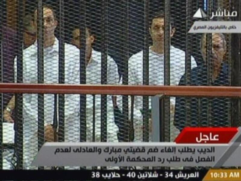 Egyptian former interior minister Habib al-Adly (R) stands along side Alaa (2nd R) and Gamal (L) Mubarak in a cage-like holding cell in the court room in the police academy.