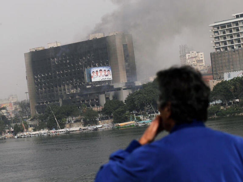An Egyptian man looks out onto a burning government building from a bridge in central.