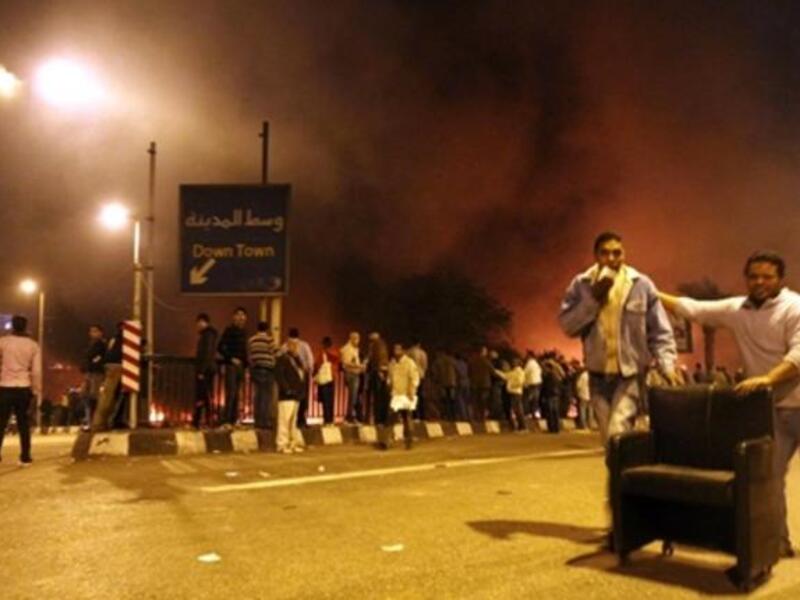 Looters roll a chair stolen from the burning headquarters of the of the ruling National Democratic party.