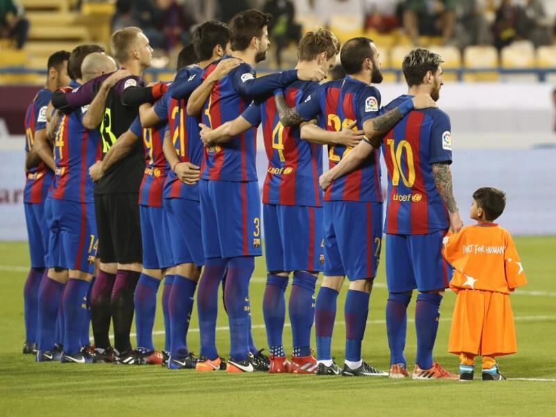 Afghan boy Murtaza Ahmadi stands with the FC Barcelona team on the pitch before the start of a friendly football match against Saudi Arabia's Al-Ahli FC on December 13, 2016 in the Qatari capital Doha. The Spanish club's last major obligation of its four year shirt sponsorship deal with Qatar Airways. KARIM JAAFAR / AFP