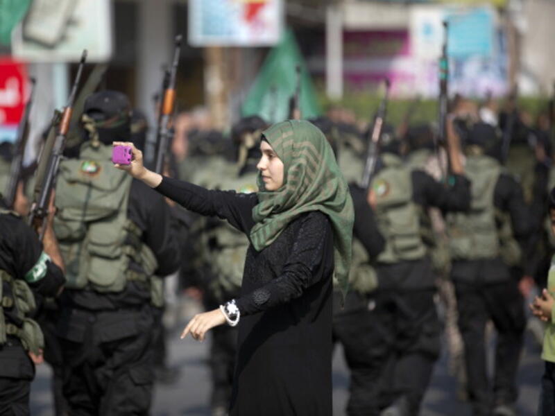 A Palestinian girl takes a photo of masked militants of Ezzedine al-Qassam Brigades, Hamas's armed wing, using her mobile phone as they parade in Jabalia refugee camp, northern Gaza Strip, on November 14, 2013, during an anti-Israel march as part of the celebrations marking the first anniversary of Israel's Operation 'Pillar of Defence'. [MOHAMMED ABED/AFP/Getty Images]