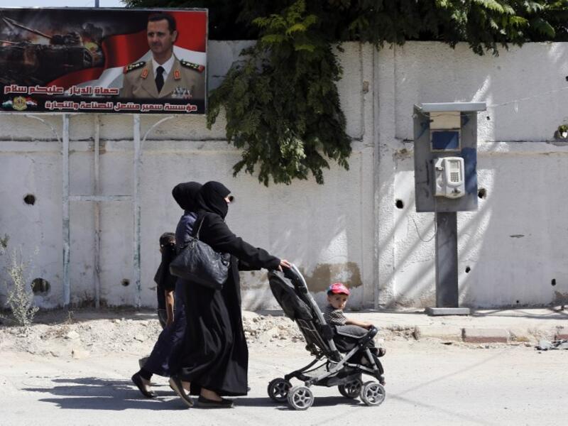 Women walks past a poster of Syrian President Bashar al-Assad during Syria's first local elections since 2011, on September 16, 2018. (LOUAI BESHARA / AFP)