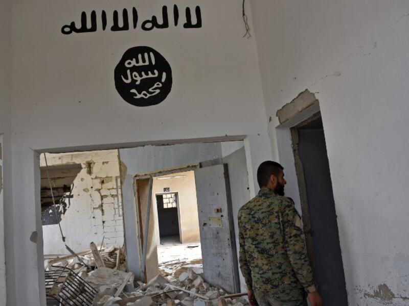 A Syrian government forces fighter walking under Islamic State (IS) group graffiti in a house in Deir Hafer on the eastern outskirts of Aleppo on March 30, 2017, after they took control of the village. (George Ourfalian/AFP)