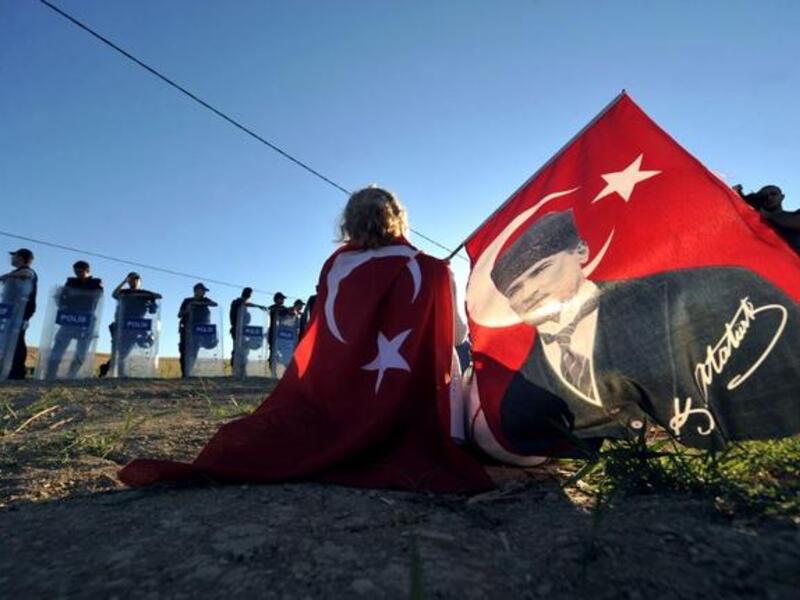 TURKEY, Silivri : Wrapped in a Turkish flag and holding another one with a portrait of Mustafa Kemal Ataturk, a protestor sits in front of police forces blocking the access to a courthouse in Silivri, near Istanbul, on August 5, 2013, where Ilker Basbug was sentenced to life imprisonment. AFP PHOTO / OZAN KOSE