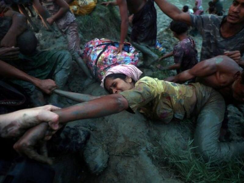 مصورون يساعدون امرأة من أقلية الروهينجا المسلمة على الخروج من نهر ناف، بعد رحلة العبور الشاقة من ميانمار إلى بنغلاديش.