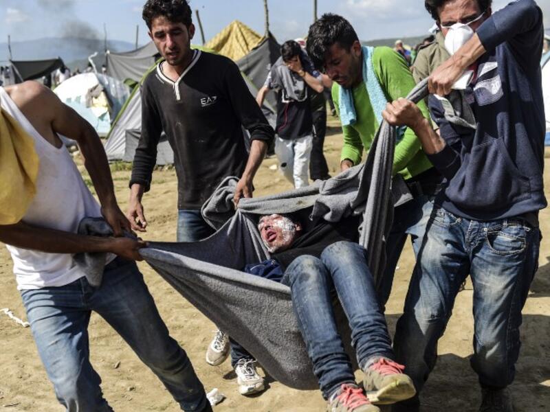 Migrants and refugees carry a man injured during clashes with Macedonian soldiers near their makeshift camp in the northern Greek border village of Idomeni, on April 10, 2016. (AFP/Bulent Kilic)