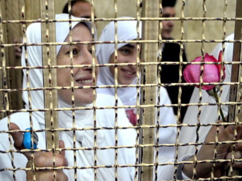 Egyptian women members of the Muslim Brotherhood hold roses as they stand in the defendants' cage dressed in prison issue white during their trial in at the court in the Egyptian Mediterranean city of Alexandria on December 7, 2013. [Getty Images]