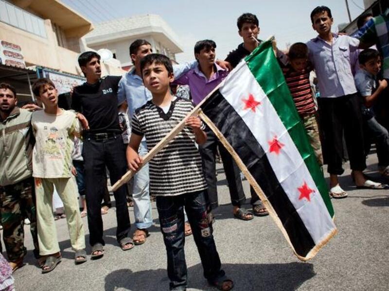 In August this year a boy holds a pre-Baath Syrian flag, that was adopted by the Syrian revolution during the uprising. (AFP PHOTO / ACHILLEAS ZAVALLIS)