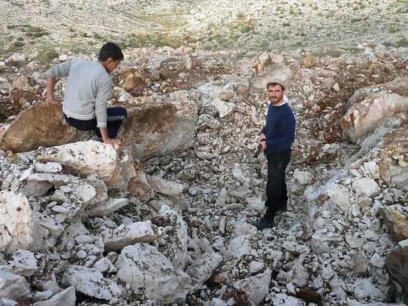 Syrian men stand inside a crater where they said a Scud missile landed near the military base of Sheikh Suleiman on the outskirts of the northwestern town of Darret Ezza on Friday. (AFP PHOTO / HERVE BAR)