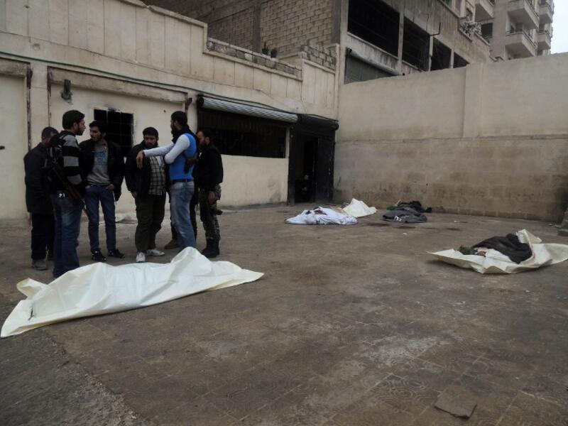 Rebel fighters talk near the bodies of the victims of a suicide bombing allegedly carried by al-Qaeda-linked group Islamic State of Iraq and the Levant's (ISIL) near the headquarters of the Army of the Mujahideen. [AFP]