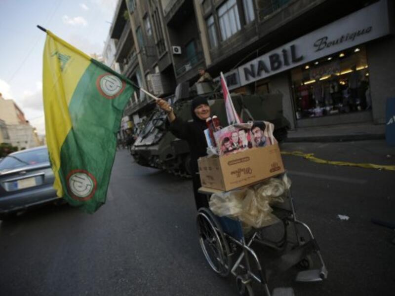 A Lebanese Shiite woman waves a Hezbollah and Amal movements flag as she pushes a cart past a Lebanese army forces checkpoint in the southern suburb of Beirut on September 23, 2013. Shells fired from Syria, where Hezbollah are fighting, hit northern Lebanese towns on Wednesday. (AFP)