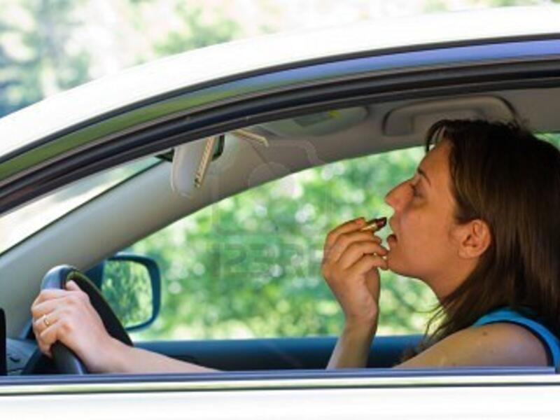 A woman applies lipstick while driving.