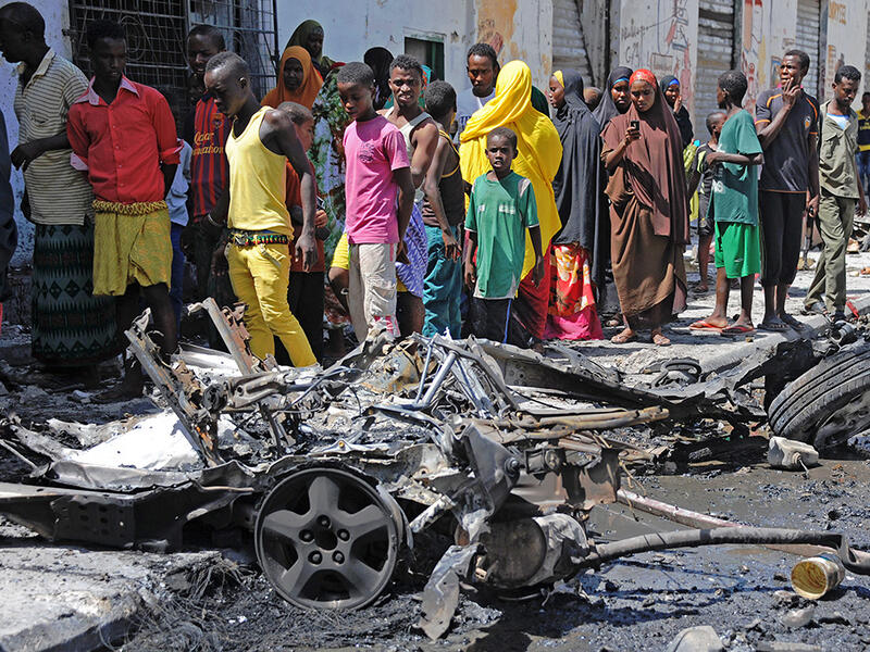Bystanders look at the wreckage of a car bomb attack in Mogadishu on April 21, 2015. (AFP/Mohamed Abdiwahab)