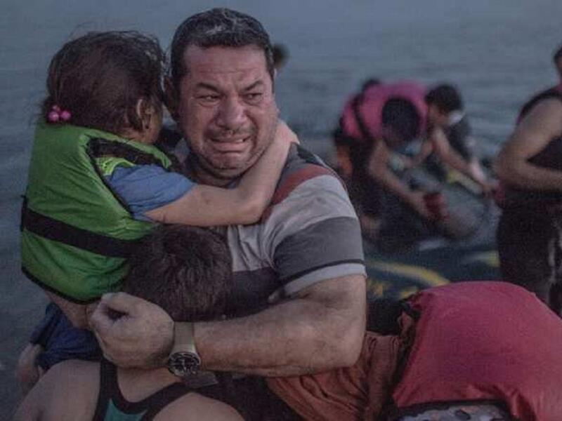 لاجئ يحتضن أولاده خلال بكائه بفرحة وصول قاربهم إلى إحدى الجزر اليونانية.