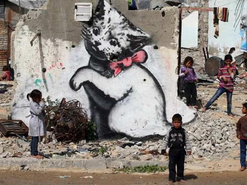 أطفال في قطاع غزة يلعبون بالقرب من بقايا منزل في حي بيت حانون، والذي تدمر بعد قتال وقع بين حركة حماس وإسرائيل عام 2014، لتنتشر رسوم على جدران المنازل، والتي قيل أن راسمها كان الرسام العالمي المجهول "بانكسي."