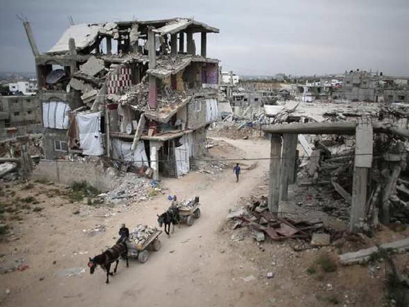 فلسطينيون يركبون عربات تجرها الحمير بين أنقاض مبان مدمرة في قطاع غزة، المباني تضررت بعد الحرب التي استمرت 50 يوماً بين إسرائيل وحماس عام 2014.