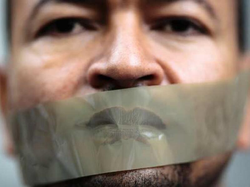 رجل يضع شريطاً لاصقاً على فمه في مظاهرة بألمانيا احتجاجاً على احتجاز الصحفي بقناة الجزيرة، أحمد منصور، من قبل السلطات الألمانية، وذلك بناءً على طلب من الحكومة المصرية، حيث تم الإفراج عنه في وقت لاحق.