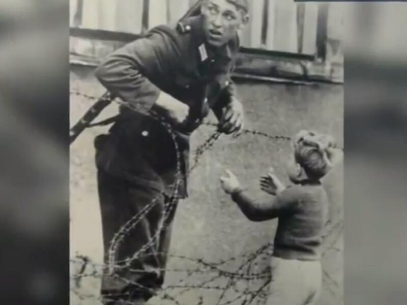 صورة لجندي من الضفة الشرقية يحاول مساعدة طفل من الضفة الغربية لألمانيا على اجتياز جدار برلين، حيث تظهر الصورة لهفة الطفل بالعودة لأهله وخوف الجندي من ضبطه في حالته الإنسانية، والذي كان لديه تعليمات آنذاك بقتل متسلقي الجدار.