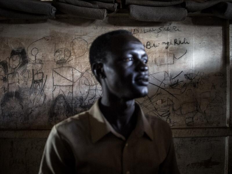 John Aremic, 20, a South Sudanese Refugee stands in front of a wall filled with drawings and writings depicting scenes from home in a building located in a transition camp for South Sudanese refugees who have just arrived in Aru. JOHN WESSELS / AFP