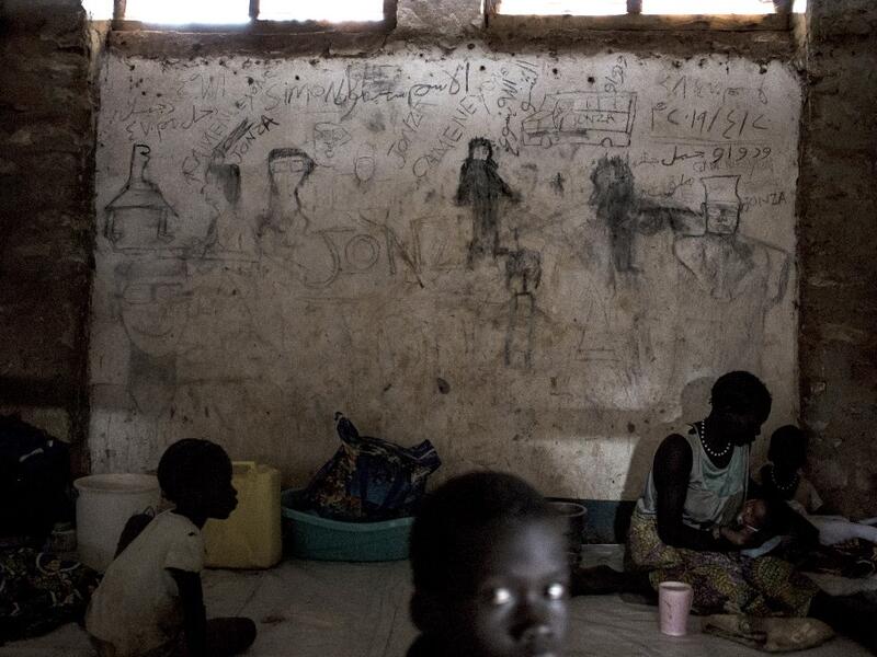 South Sudanese refugees sit in front of a wall filled with drawings and writings depicting scenes from home in Aru JOHN WESSELS / AFP