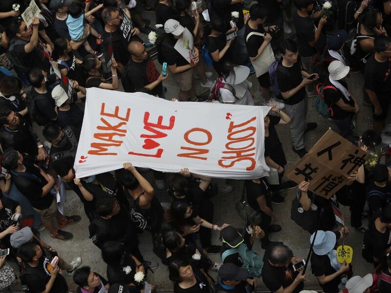 People carry a banner reading "Make love no shoot" in reference to police firing on protesters on June 12, as thousands of protesters dressed in black take part in a new rally against a controversial extradition law proposal in Hong Kong  Dale DE LA REY / AFP