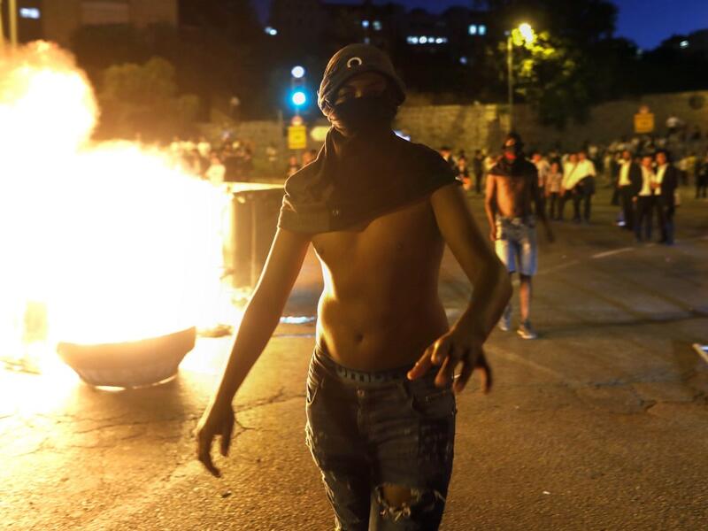 A masked Israeli member of the Ethiopian community walks past a burning barrier blocking the main entrance to Jerusalem, to protest the killing of Solomon Tekah, a young man of Ethiopian origin who was killed by an off-duty police officer.  MENAHEM KAHANA / AFP