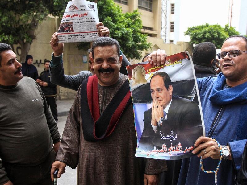 Egyptians pose for a picture with a newspaper front page and a poster of President Abdel Fattah al-Sisi outside a school in the second city of Alexandria during voting in a referendum on constitutional amendments on the first day of the three-day poll, on April 20, 2019. Tarek ABDEL HAMID / AFP
