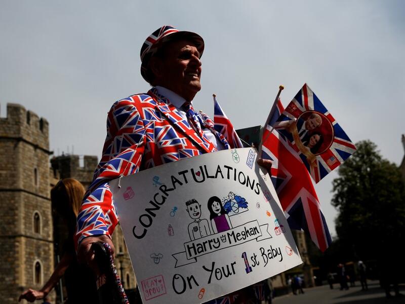 Royal super fan Terry Hutt, wearing a Union-flag themed suit, holds a congratulatory banner as he walks outside Windsor Castle in Windsor, west of London on May 7, 2019, the day after the announcement that Britain's Meghan, Duchess of Sussex had given birth to a son. ADRIAN DENNIS / AFP