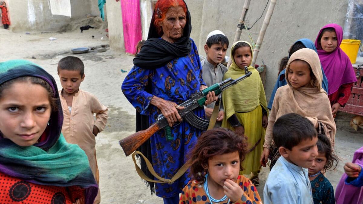 In this photograph taken on April 22, 2019, Afghan woman Niaz Bibi (C in blue),70, holds a weapon as she stands among her orphaned children and grandchildren at their home in the Kot district of the Nangarhar province. NOORULLAH SHIRZADA / AFP