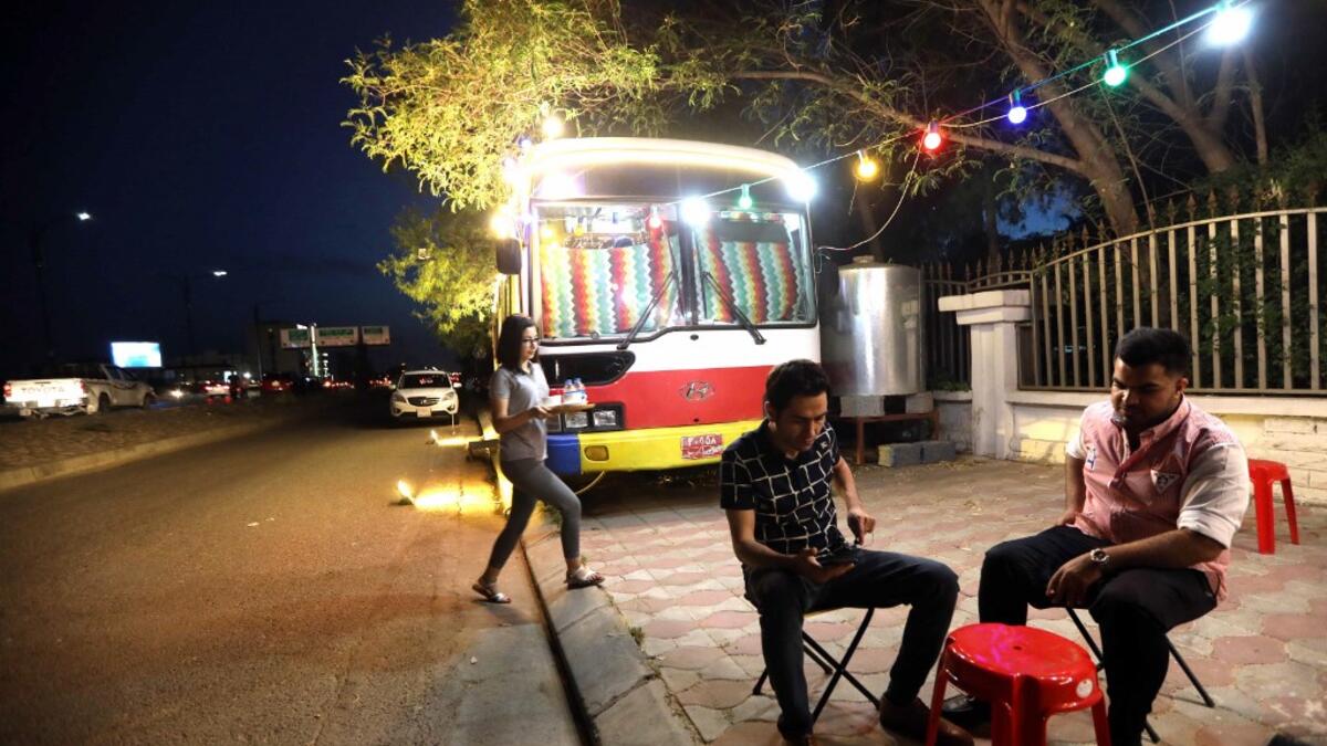 Kani Jalil, a 22-year-old Iraqi Kurdish woman who runs with her husband "The Bus Cafe Erbil" in Arbil, the capital of Iraq's Kurdish autonomous region, serves drinks to two clients seated outside her bus late on June 7, 2019, on the long weekend of the Eid al-Fitr holiday which marks the end of the holy fasting month of Ramadan.  SAFIN HAMED / AFP