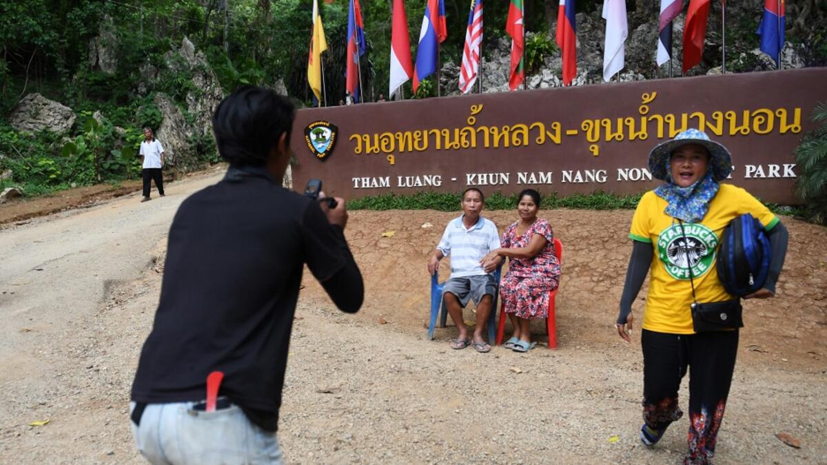 This picture taken on June 13, 2019 shows visitors posing for photos near the entrance of the Tham Luang cave, in which 12 boys from the "Wild Boars" football team and their coach were trapped last year, in the Mae Sai district of Chiang Rai province. Lillian SUWANRUMPHA / AFP