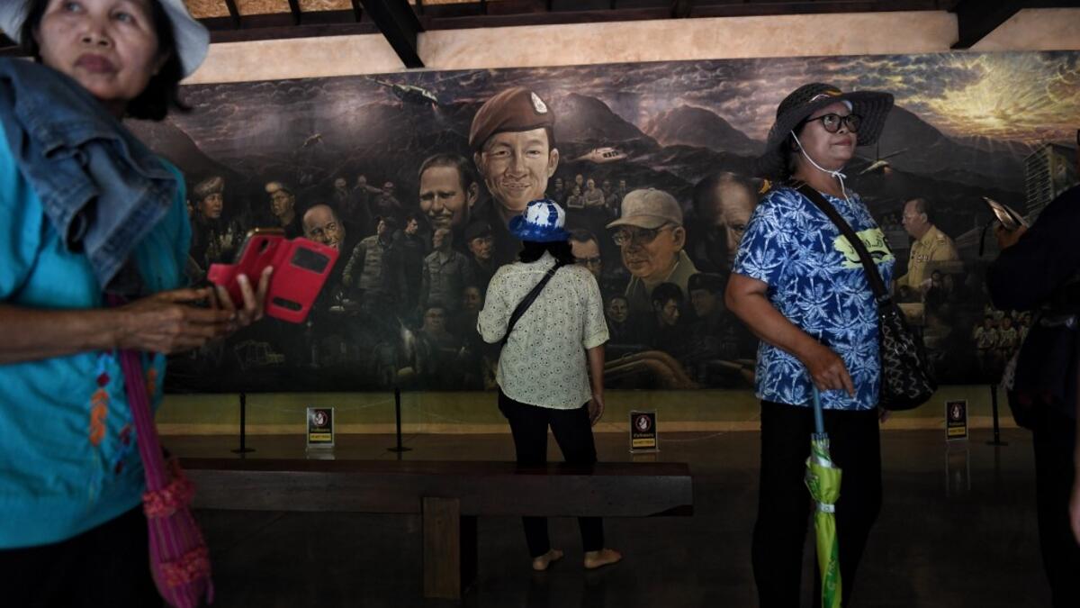 This picture taken on June 13, 2019 shows visitors taking photos in front of a mural, illustrating the efforts to rescue of the 12 boys from the "Wild Boars" football team and their coach after they were trapped in the Tham Luang cave last year, at the cave's visitor centre in the Mae Sai district of Chiang Rai province. Lillian SUWANRUMPHA / AFP