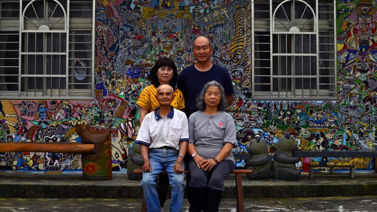 This picture taken on May 21, 2019 shows Hakka graffiti artist Wu Tsun-hsien (top R) posing with his family in front of their home in the Taiwanese village of Ruan Chiao. Nestled in the mist-covered foothills of Taiwan's central mountain range, Ruan Chiao village is virtually devoid of young people, but artist Wu Tsun-hsien is coaxing the Instagram generation back by transforming local homes into a canvas of colour. Sam YEH / AFP