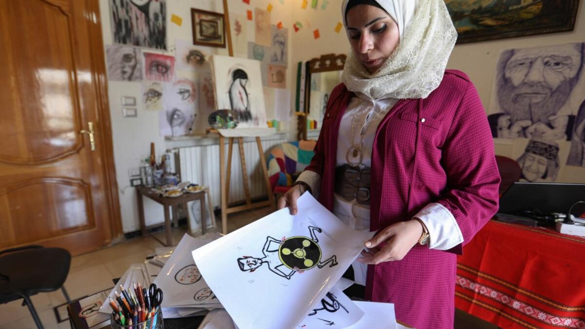 Syrian Cartoonist Amani al-Ali shows one of drawings, depicting a naked President Bashar al-Assad covering his lower torso with a chemical weapons hazard symbol, at her home studio in the city of Idlib in the eponymous northwestern province Omar HAJ KADOUR / AFP