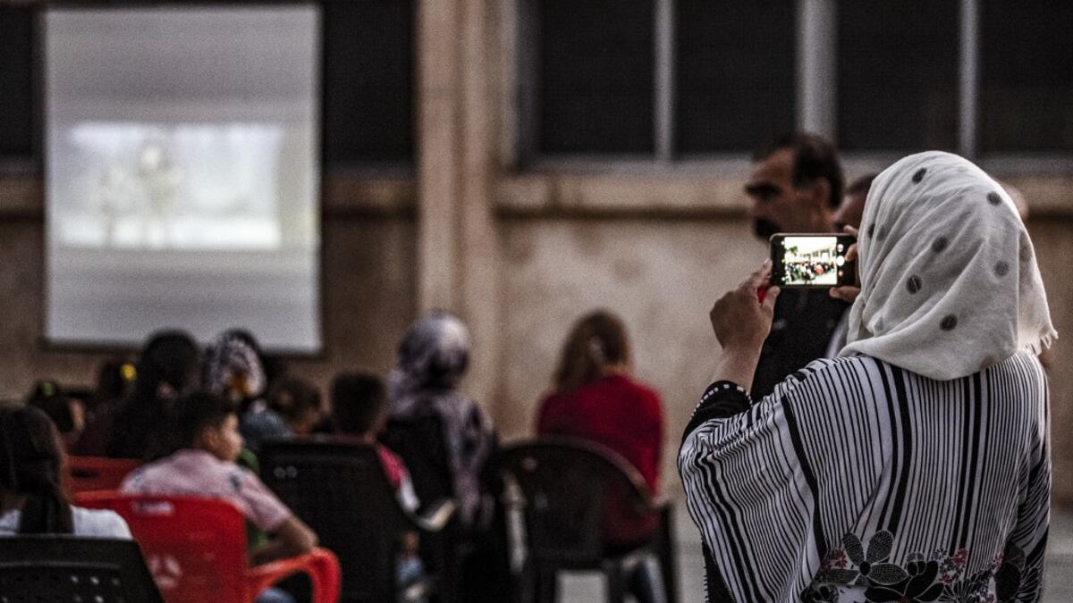 A woman uses a cell phone to shoot a video of children attending a film screening as part of the mobile cinema "Komina Film" initiative organised by Syrian-Kurdish filmmaker Shero Hinde, at a school yard in the village of Shaghir Bazar, 55 kilometres southest of Qamishli in the Kurdish-populated areas of northeastern Syria's Hasakeh province, on July 28, 2019. DELIL SOULEIMAN / AFP