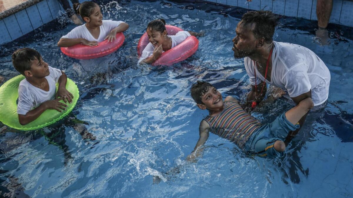 A trainer helps a Palestinian amputee child swim during a summer camp origanized by the Palestinian Children's Relief Fund (PCRF) in the town of Khan Yunis in the southern Gaza strip on August 3, 2019.  SAID KHATIB / AFP