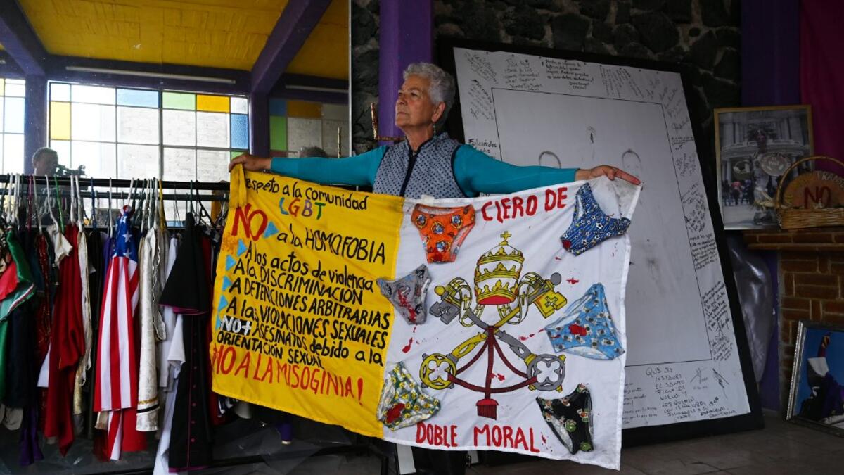 Mexican activist Julia Klug poses with a banner against homophobia in Mexico City on August 08, 2019. Pork masks, a giant magnifying glass made with a sewing drum, and hundreds of costumes are included in the collection of Julia Klug. RODRIGO ARANGUA / AFP