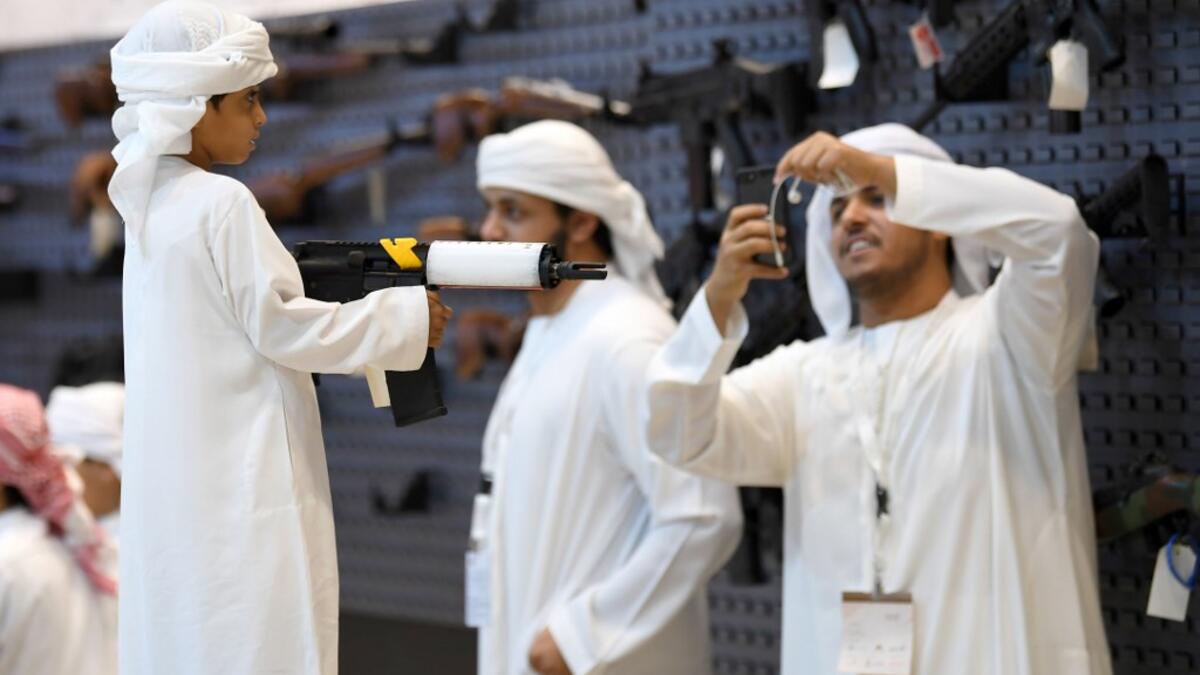 A boy poses for a picture with an assault rifle taken by another visitor on his phone during the Abu Dhabi International Hunting and Equestrian exhibition (ADIHEX) in the UAE capital Abu Dhabi on August 31, 2019.  KARIM SAHIB / AFP