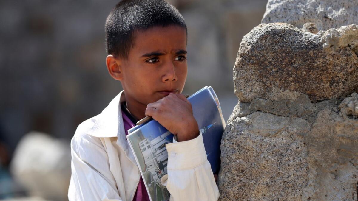 A Yemeni boy holds his notebooks as school children attend an open-air class under a tree near their unfinished school  Ahmad AL-BASHA / AFP