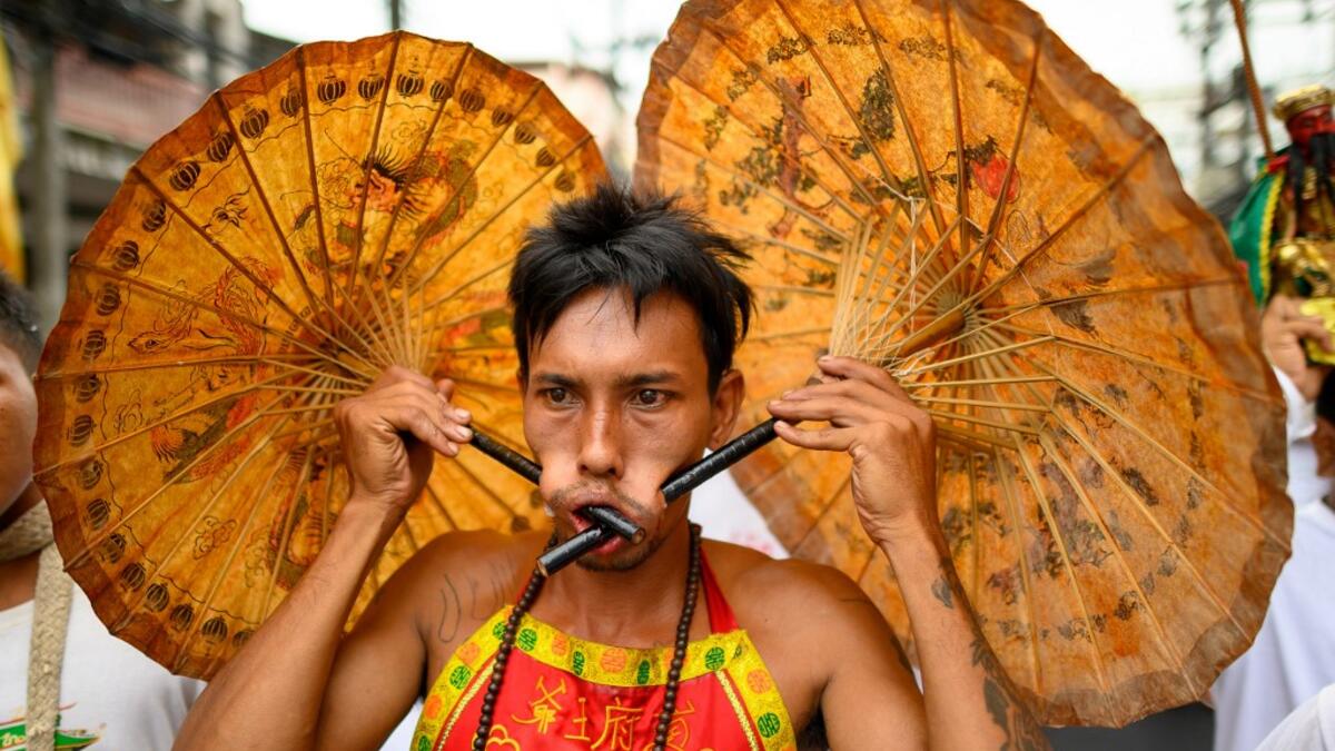 A devotee of a Chinese shrine with two umbrellas pierced through his cheeks takes part in a procession during the annual Vegetarian Festival in Phuket on October 5, 2019. Mladen ANTONOV / AFP