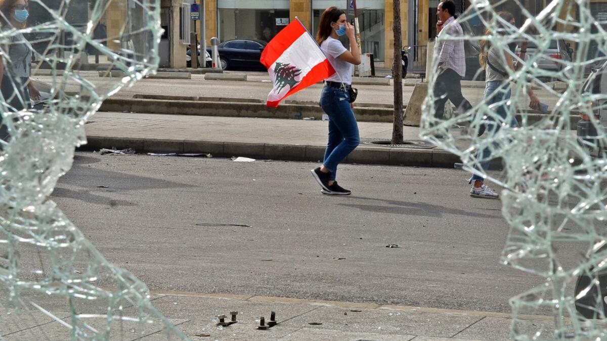 A masked woman walks with a Lebanese national flag tucked into her pocket past a broken window along a street in the centre of the capital Beirut on October 18, 2019 amidst ongoing protests against dire economic conditions. Public anger has simmered since parliament passed an austerity budget in July to help trim a ballooning deficit and flared on October 17 over new plans to tax calls on messaging applications such as WhatsApp, forcing the government to axe the unpopular proposal. AFP