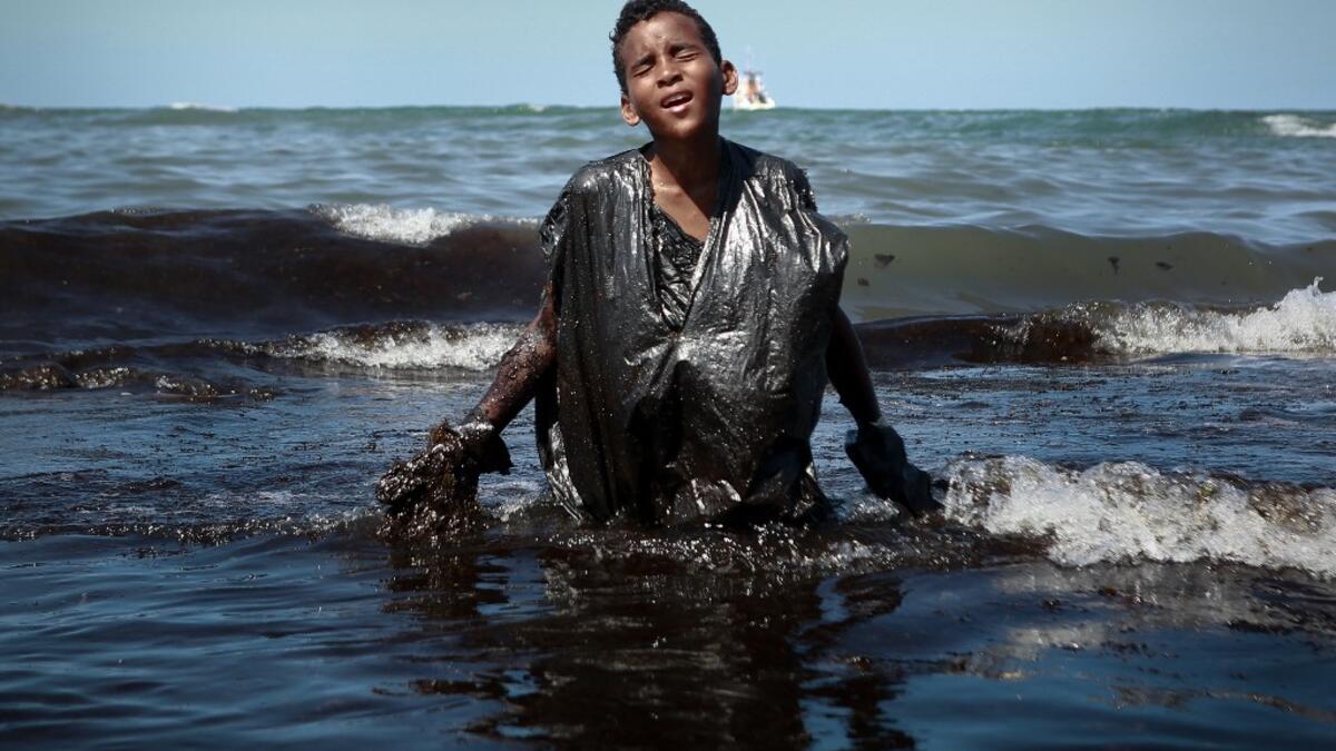 A boy walks out of the sea while removing oil spilled on Itapuama beach located in the city of Cabo de Santo Agostinho, Pernambuco state, Brazil, on October 21, 2019. LEO MALAFAIA / AFP