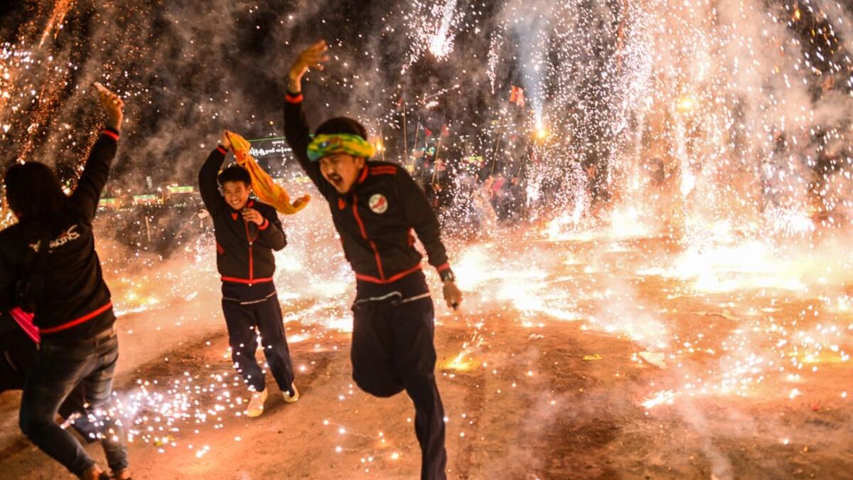 This picture taken on November 5, 2019 shows participants celebrating as fireworks explode after they released a hot-air balloon attached with fireworks during the Tazaungdaing Lighting Festival at Taunggyi in Myanmar's northeastern Shan State. Brightly coloured balloons with hundreds of homemade fireworks woven into their frames are sent soaring into the night sky, showering down cascades of sparks onto adoring crowds in the annual Taunggyi fire balloon festival. Ye Aung THU / AFP