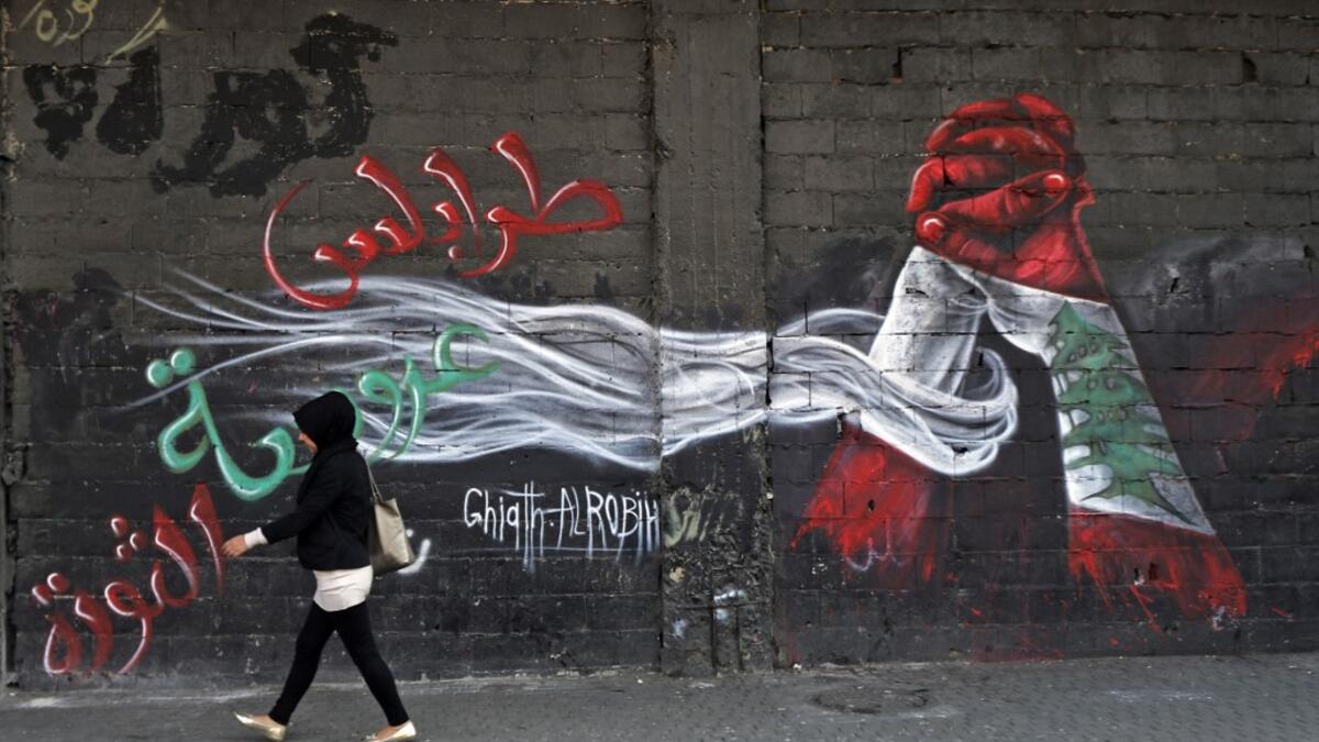A woman walks past a graffiti drawn on the wall of a building at the al-Nour Square in the northern port city of Tripoli on November 7, 2019. An unprecedented protest movement has gripped Lebanon since October 17, demanding an overhaul of a political class that has remained largely unchanged since the end of the country's 1975-1990 civil war. In the northern city of Tripoli, where mobilisation has been relentless since the protests erupted on October 17, demonstrators took down politicians' portraits from c