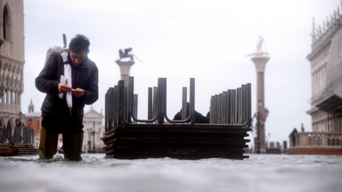 A man prepares a cigarette as he walks in the water of the flooded St. Mark's Square, on November 15, 2019 in Venice, two days after the city suffered its highest tide in 50 years. Flood-hit Venice was bracing for another exceptional high tide on November 15, as Italy declared a state of emergency for the UNESCO city where perilous deluges have caused millions of euros worth of damage. Filippo MONTEFORTE / AFP