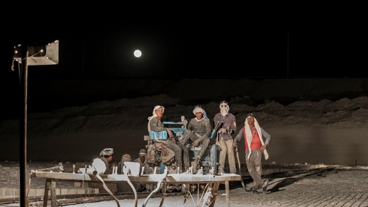 Labourers, some wearing protective gear, pose for a picture by a full moon while working late at night at the "White Mountain" limestone extraction quarry site near Egypt's southern city of Minya, some 265 kilometres south of the capital, on November 13, 2019. Covered in fine white dust, labourers at the so-called "White Mountain" off Minya toil in shifts amidst brutal conditions with little workplace safety for paltry pay. They handle dangerous machinery with finesse, and shrug off the dangers of a job whe