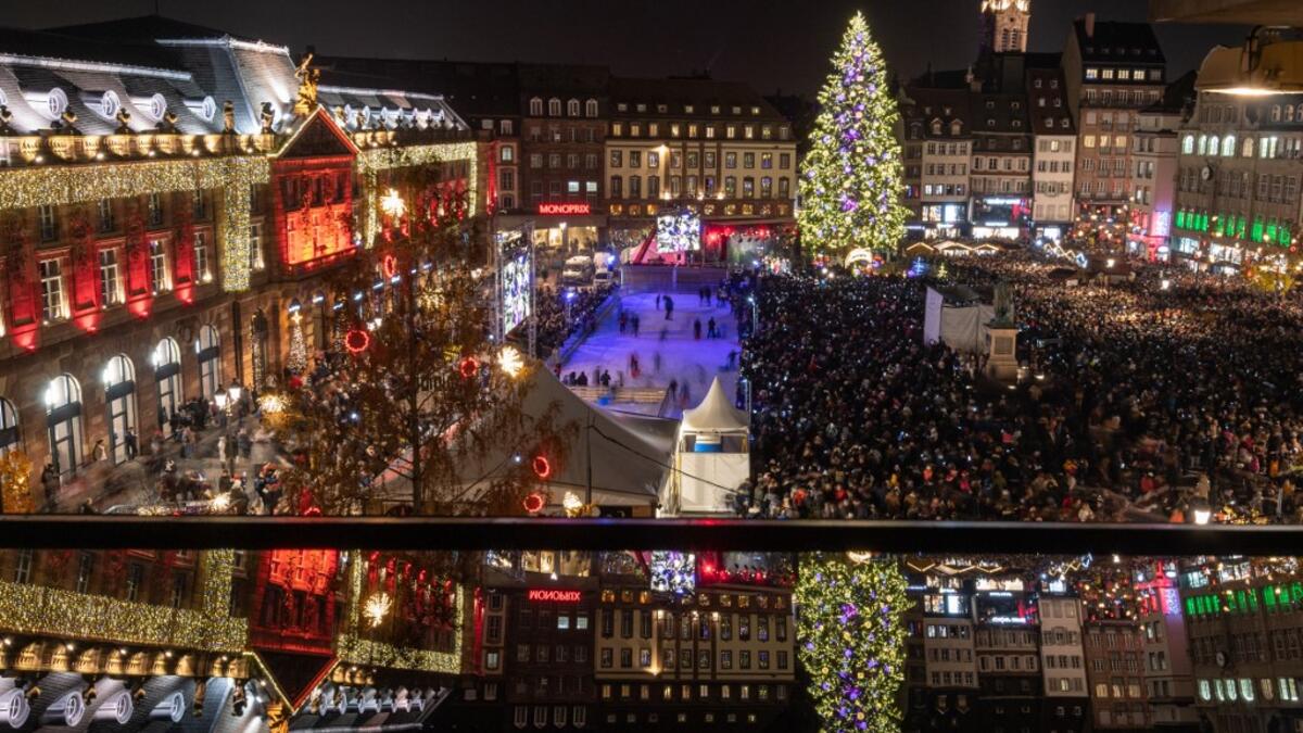This picture shows a reflected view of the city's illuminated main square and Christmas tree as people gather on the opening day of the 450th traditional Christmas market in Strasbourg, eastern France, one year after the deadly attack that killed five people.  PATRICK HERTZOG / AFP